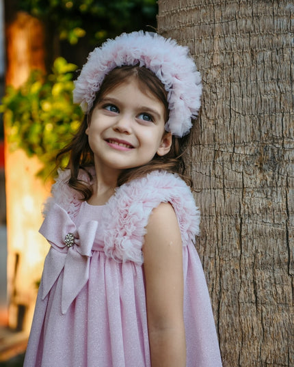 Pembe simli kumaşlı, omuz fırfırlı, fiyonklu kız çocuk abiyesi, pembe tüllü taçla yan pozda