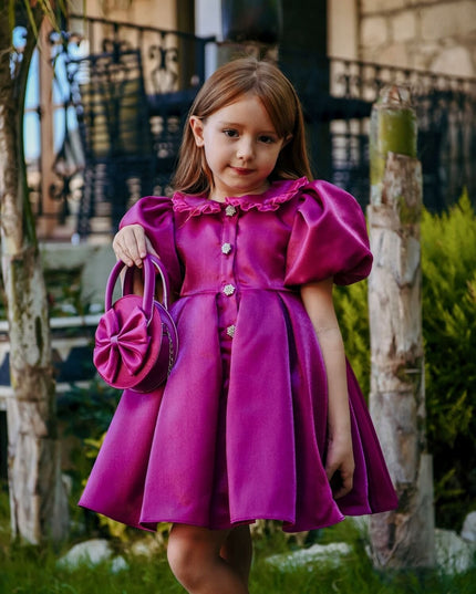 Kız çocuk için fuchsia rengi kısa abiye elbise, puf kollu yaka, ön düğme detayı ve eşleşen fiyonk çantalı